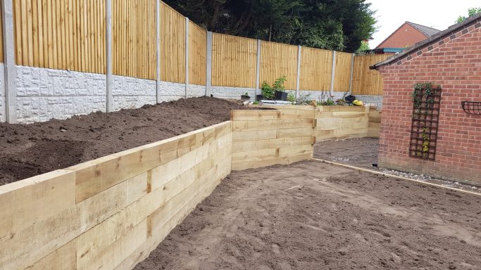 Garden landscape with wooden planters and a sandy area, surrounded by wooden fencing.