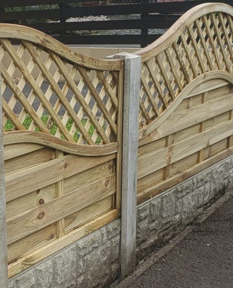 Decorative wooden fence with lattice design and stone base, featuring curved top sections.