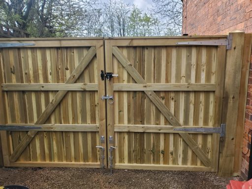 Wooden double gates with diagonal slats and metal fittings, set in a brick wall.
