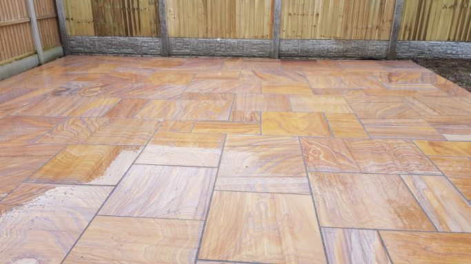 Patterned terracotta patio tiles in a rectangular layout, surrounded by wooden fencing.