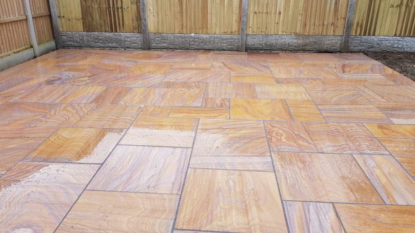 Patterned patio paving with warm-toned tiles in a garden setting.