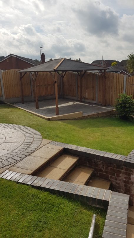 Gardens with a patio area, wooden gazebo, steps, and a fenced grassy space.