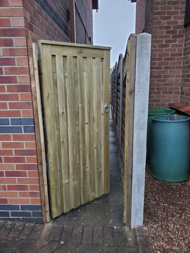 A wooden gate in a narrow pathway between brick buildings.