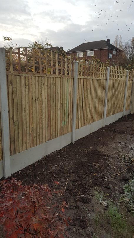 A wooden fence with concrete posts and a landscaped garden in the background.