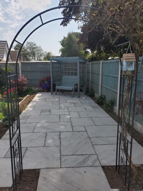 Stone patio with an arch entrance, bench, and surrounding greenery.