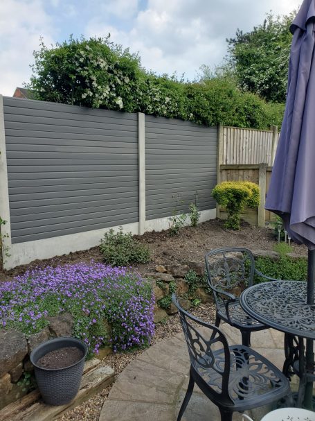 Garden scene featuring a grey fence, purple flowers, and outdoor seating.