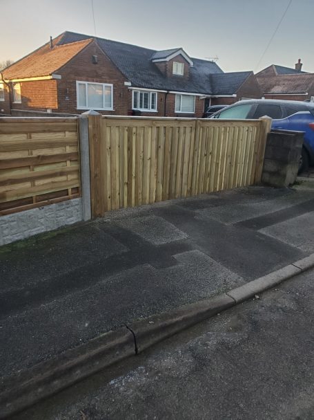 Wooden fence next to a driveway leading to a brick house on a quiet street.
