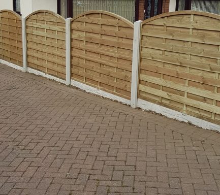 Wooden fence panels with rounded tops on a paved surface.