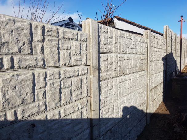 Textured concrete boundary wall under a clear blue sky.