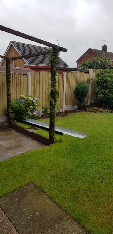 Garden featuring a lawn, wooden pergola, and shrubs against a cloudy sky.