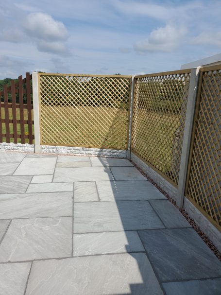 A stone patio corner with decorative lattice fencing and grassy fields in the background.