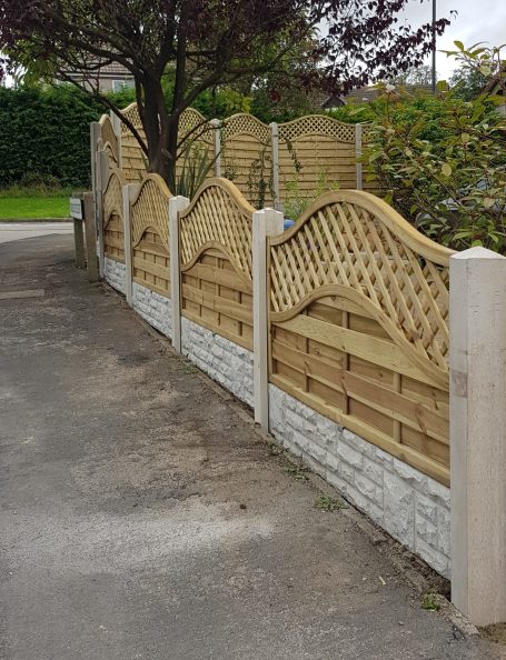 Wooden fence with decorative top, bordered by green grass and trees.