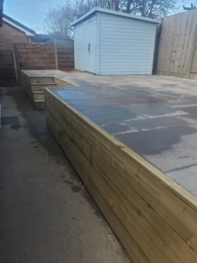 Wooden decking area adjacent to a shed, with an elevated platform on one side.
