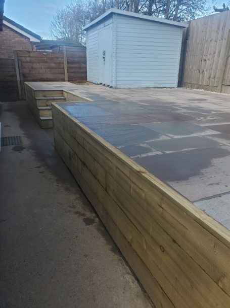 A wooden deck area with steps beside a shed in a garden setting.