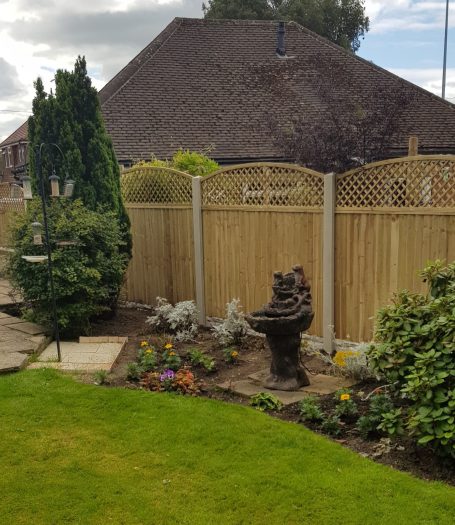 Garden with a fountain, flower beds, and a wooden fence in a residential area.