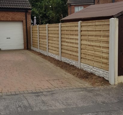 A wooden fence runs alongside a paved driveway in a residential area.