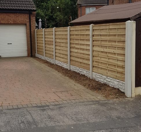 A wooden fence alongside a paved driveway and garage.