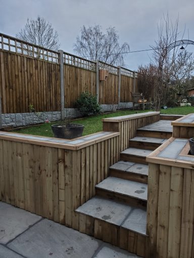 A landscaped garden with wooden steps and stone paving, surrounded by wooden fencing.