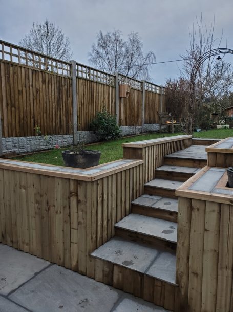 Wooden steps leading up to a landscaped garden with stone walls and plants.
