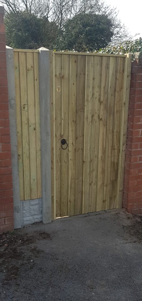 Wooden garden gate with a circular handle, set within brick walls.