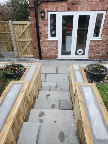 Stone steps with wooden borders, leading to a patio and entrance door. Planters on either side.