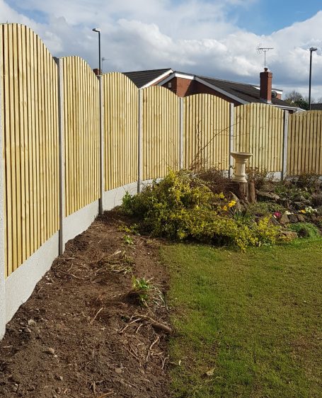 Wooden fence curving around a garden with a patch of grass and plants.