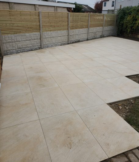 Paved outdoor area with large light-coloured tiles and a wooden fence in the background.