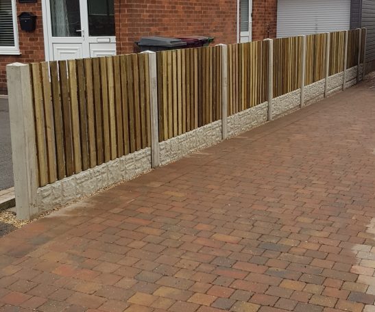 Wooden fence panels on concrete posts beside a paved driveway.
