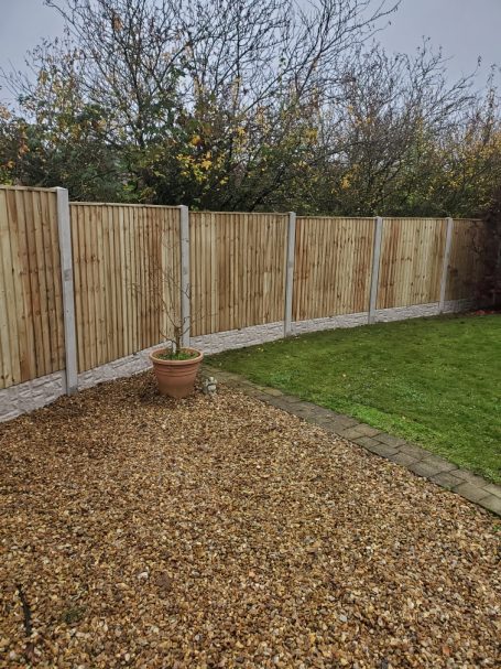 Wooden fence surrounding a garden with a gravel area and a potted plant.