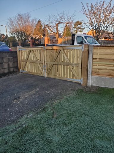 Wooden double gates set in a stone wall, with a frosty lawn and trees in the background.