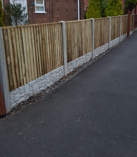 Wooden fence with vertical slats alongside a paved pathway and stone base.