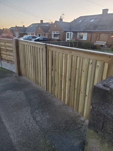 Wooden gate leading to residential houses, bordered by a wooden fence.