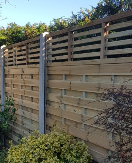 Wooden fence with horizontal slats and greenery above.