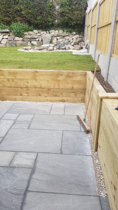 Patio with stone paving, beside wooden fencing and a grassy area.