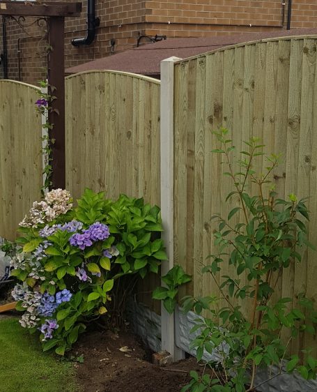Wooden fence corner with blooming shrubs and flowers in a garden setting.
