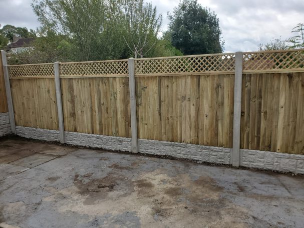 Wooden fence with lattice top, set against a cloudy sky and grassy area.