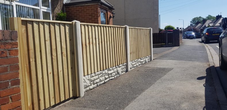 A wooden fence adjoining a gravel pathway alongside a road.
