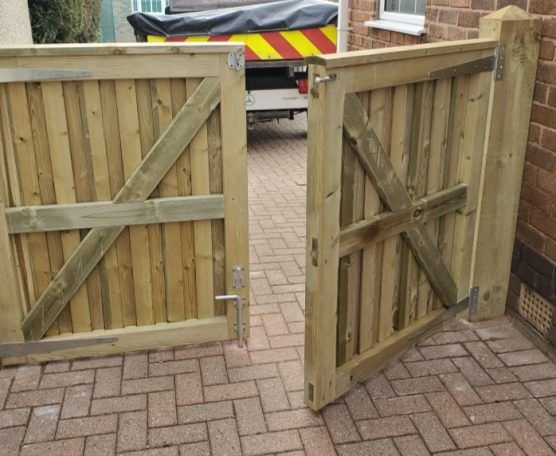 Two wooden gates swing open on a paved pathway beside a brick wall.