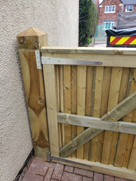 Close-up of a wooden garden gate with metal latch against a brick pathway.