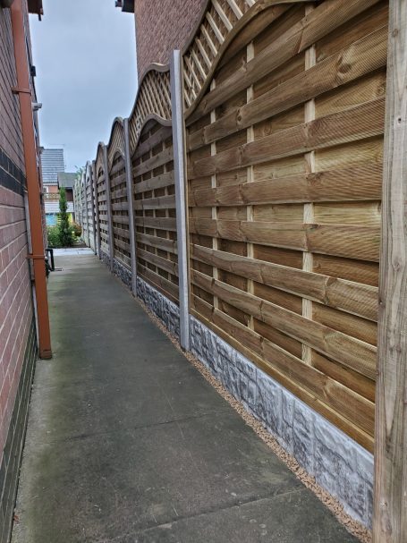 Narrow pathway between wooden fences, leading towards a brighter area.