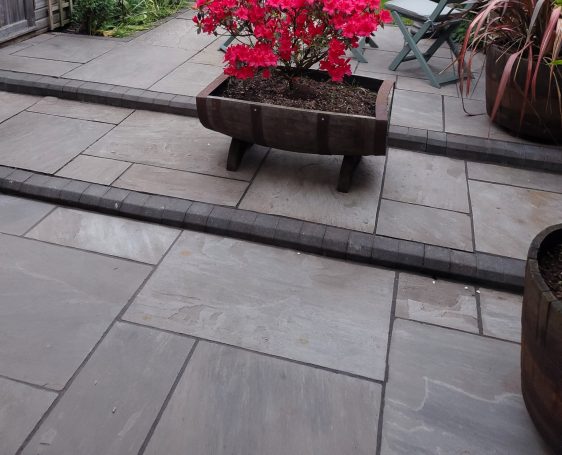 Paved patio with a flower pot containing vibrant pink flowers.