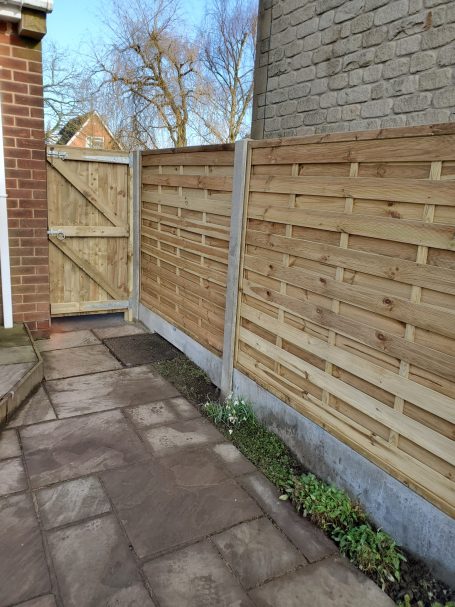 Wooden fence and gate along a stone pathway, with grass and plants at the base.