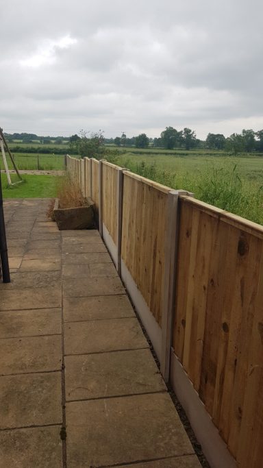 Wooden fence enclosing a patio area, overlooking a grassy field and cloudy sky.