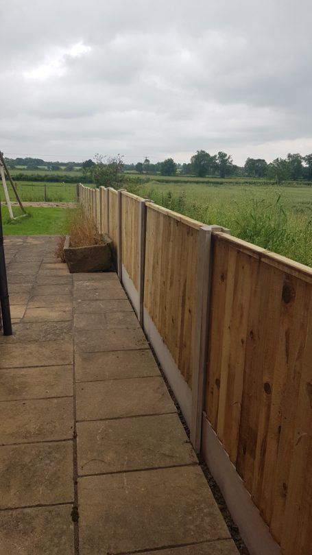 Wooden fence on a patio overlooking a grassy field under a cloudy sky.