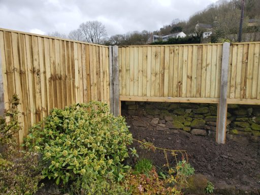 Wooden fencing with concrete posts, surrounded by a garden area and cloudy sky.