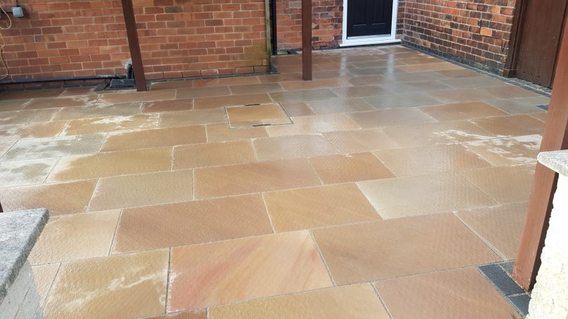 Paved patio area with large sandstone slabs and a brick wall backdrop.